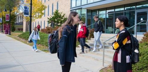 Two students talking, while others pass by on the quad